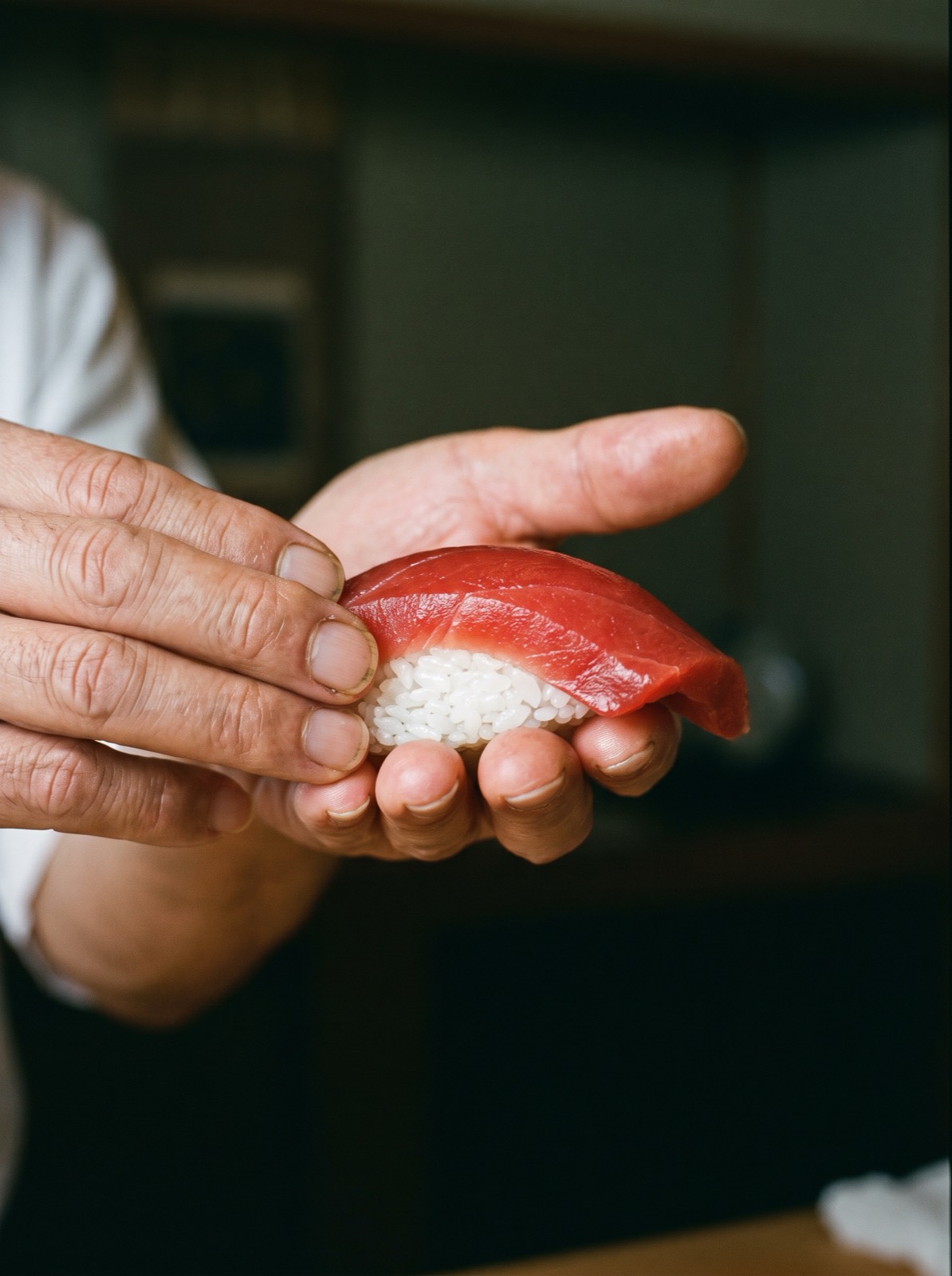 A chef’s hands closing around rice and fish at the board.