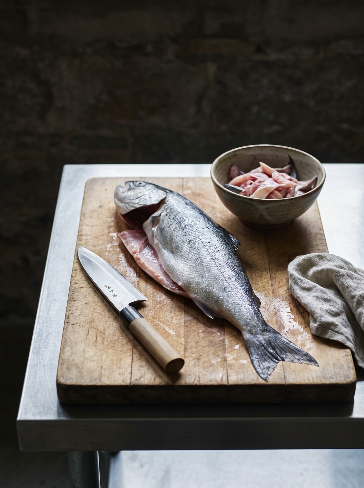 A side board with fish being broken down out of sight of the counter.