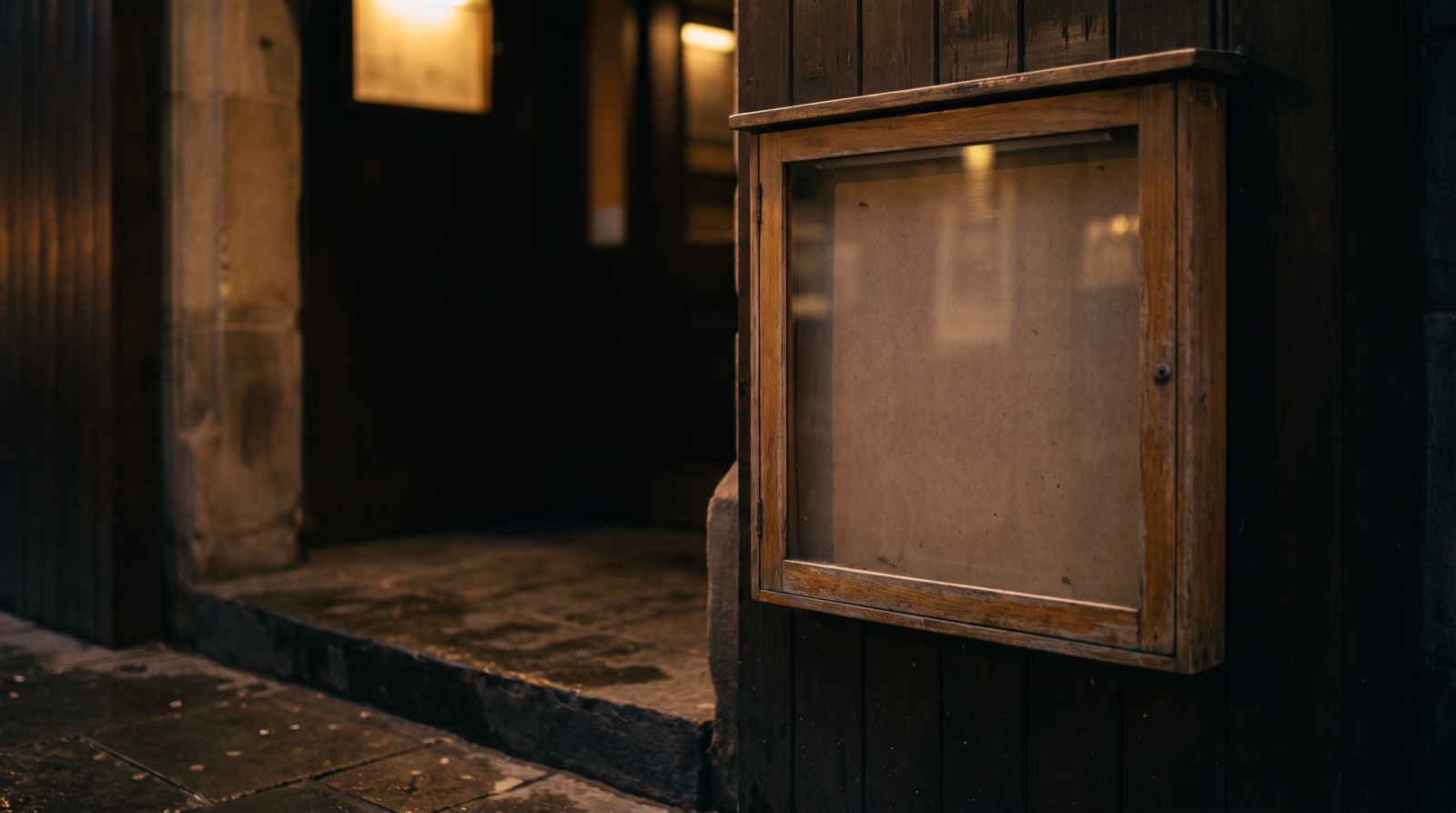 An empty glass-fronted display case on a wall beside a doorway, nothing inside it.