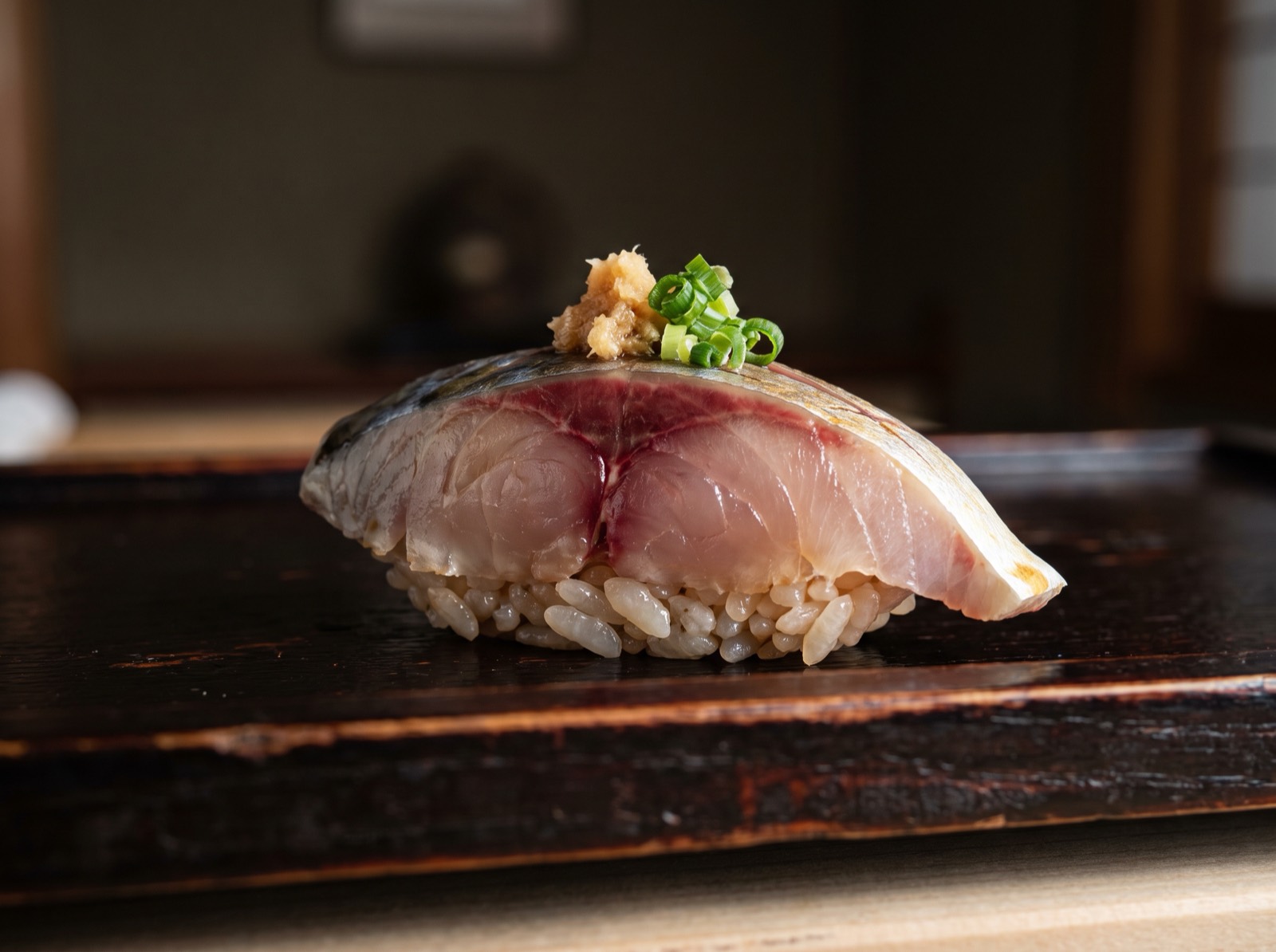 Aji nigiri topped with grated ginger and sliced spring onion.