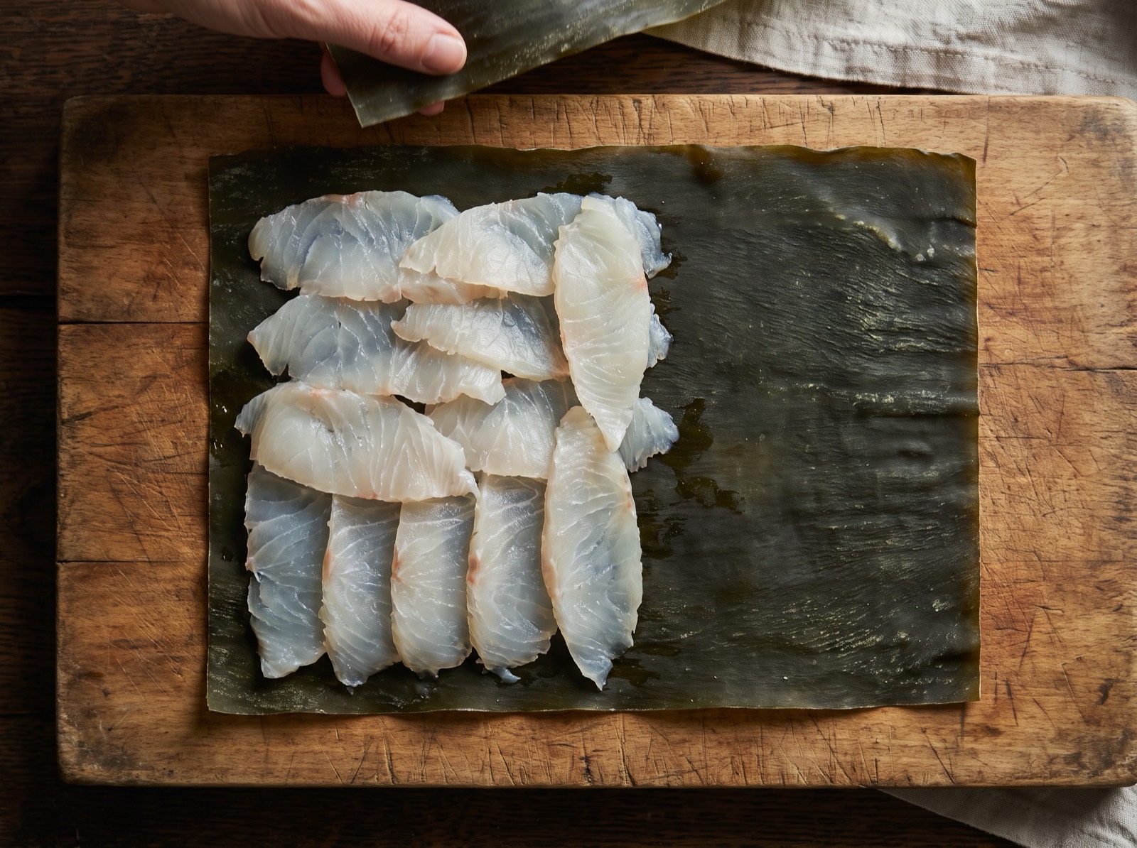Kobujime, thin slices of white fish laid over a sheet of kelp, not yet sandwiched.