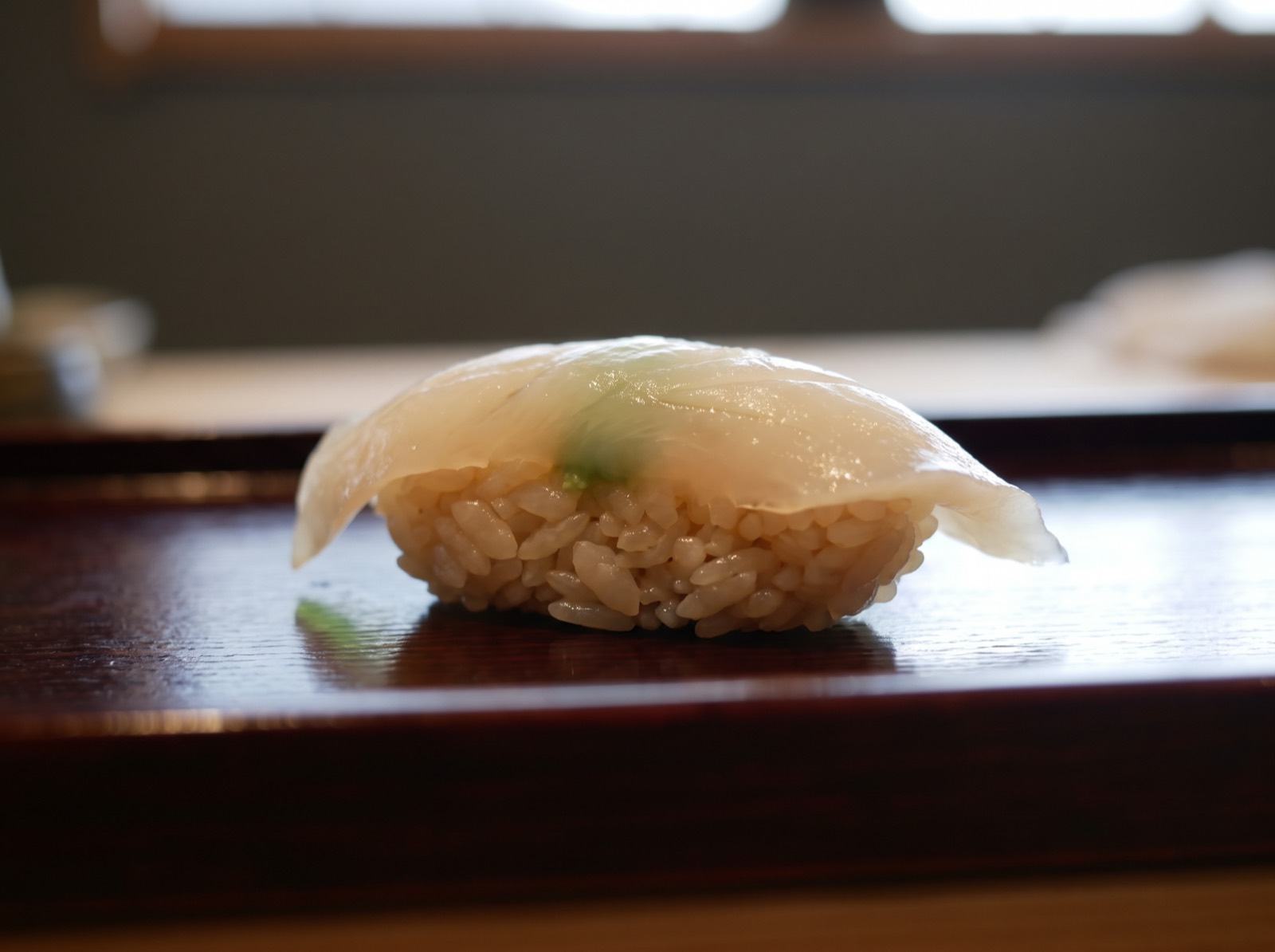 Tairagai nigiri, sliced so thin the wasabi beneath shows through as a faint shadow.