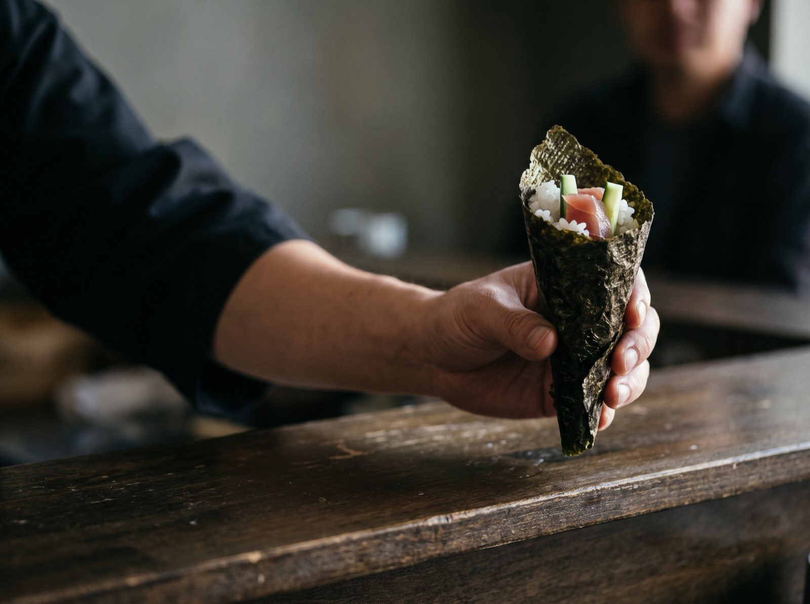 A hand roll, cone-shaped, passed across the counter.