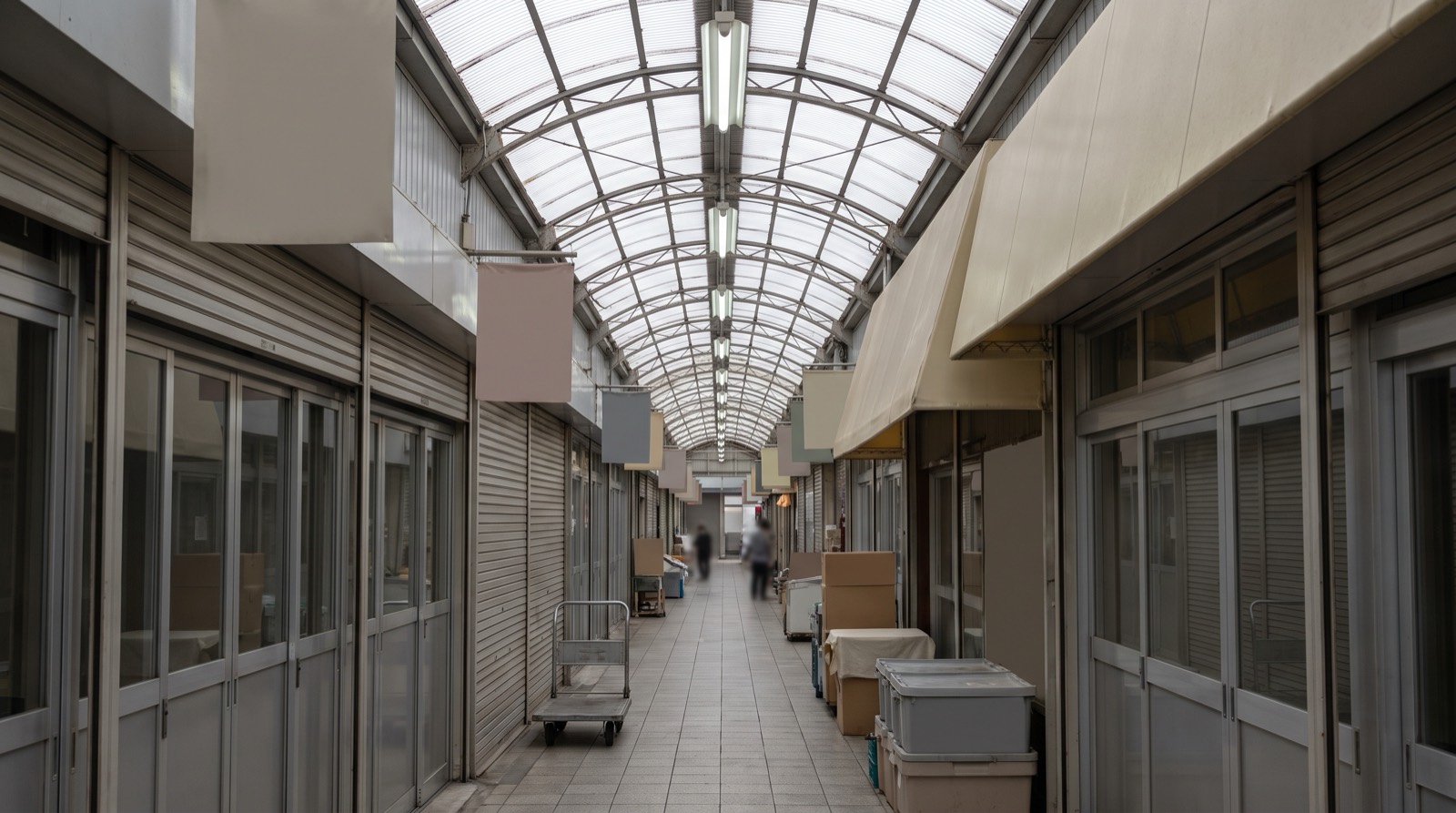 A covered Japanese shopping street in the late morning, shutters half up.
