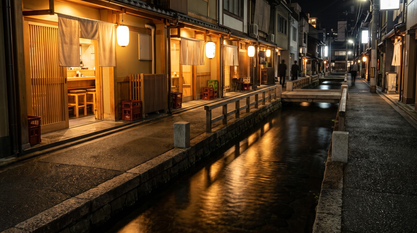 A narrow canal-side lane at night, lit frontages doubled in the water.