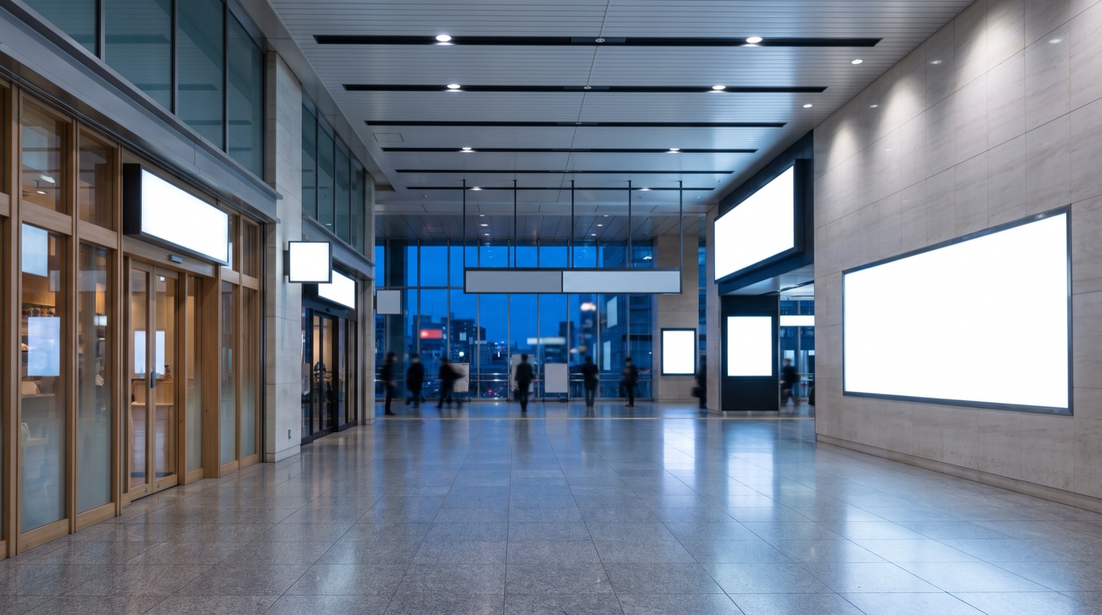 A large station concourse in the evening, blank information panels ranked along a wall.