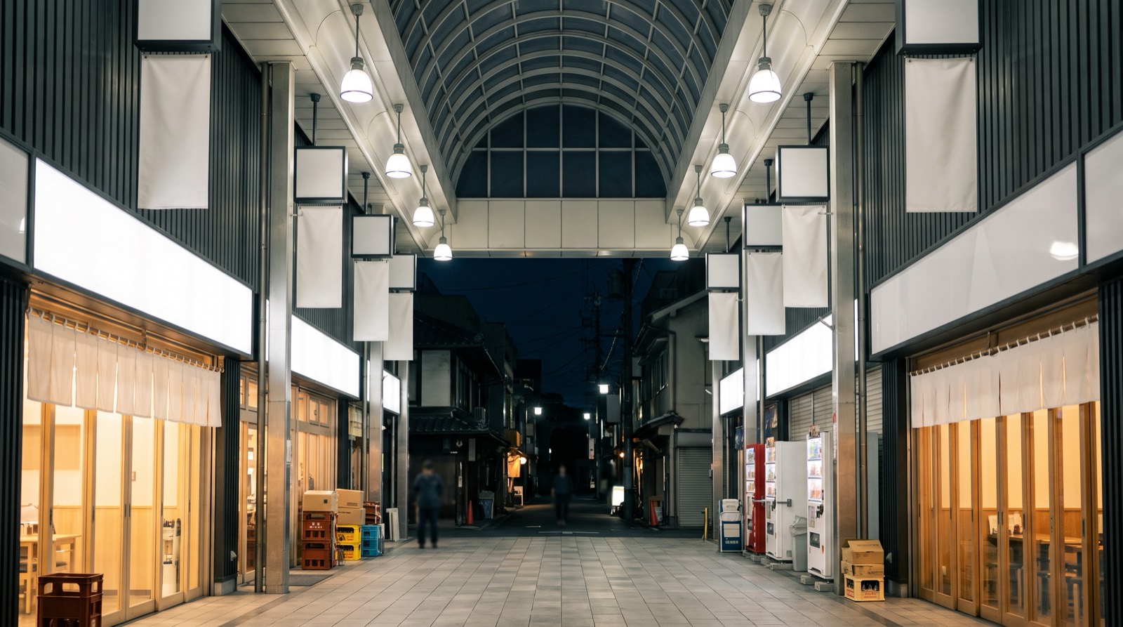 The end of a covered arcade at night, opening into an unroofed side street.