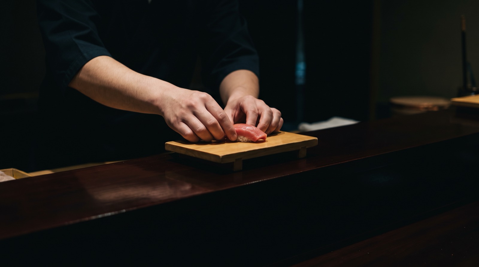 A single piece of nigiri being set down on the counter tray, seen across the counter.