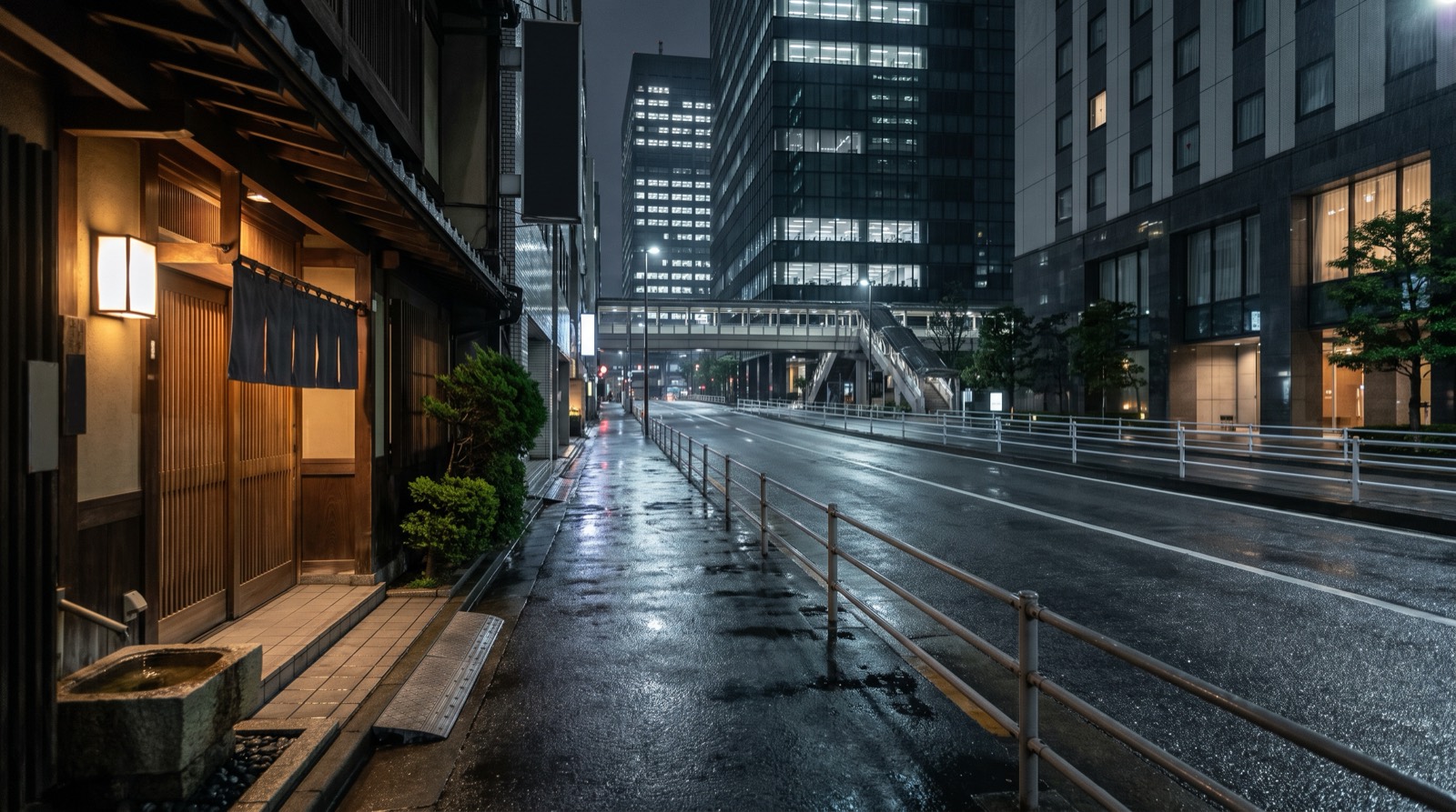 A sloping office-district street at night, a low restaurant frontage below the towers.