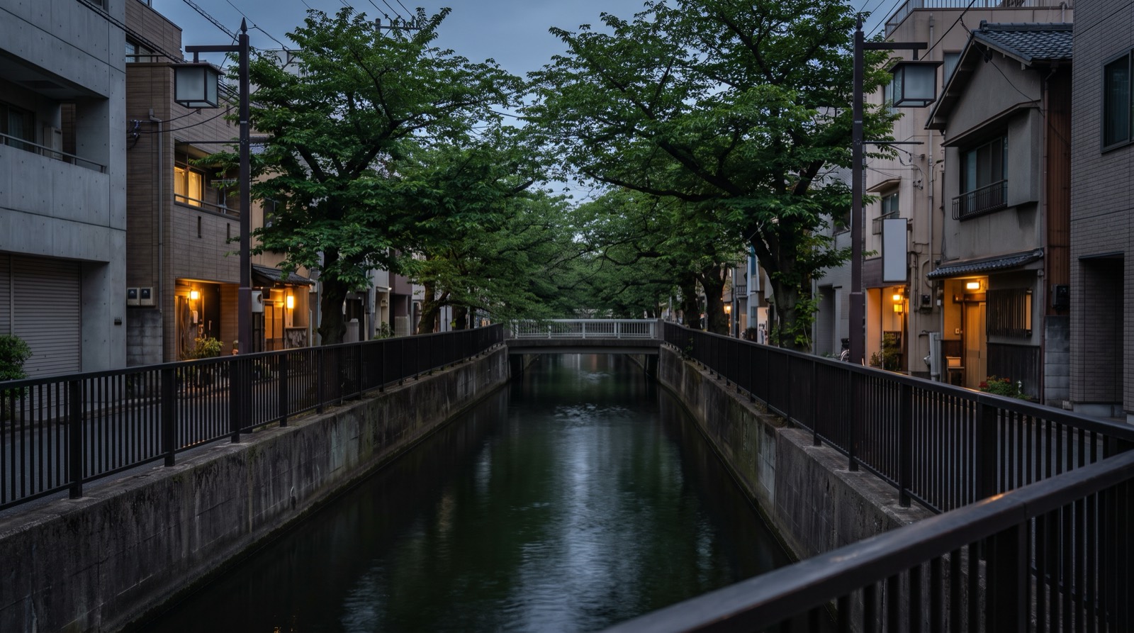 A narrow canal between low buildings at early evening, lit windows on both banks.
