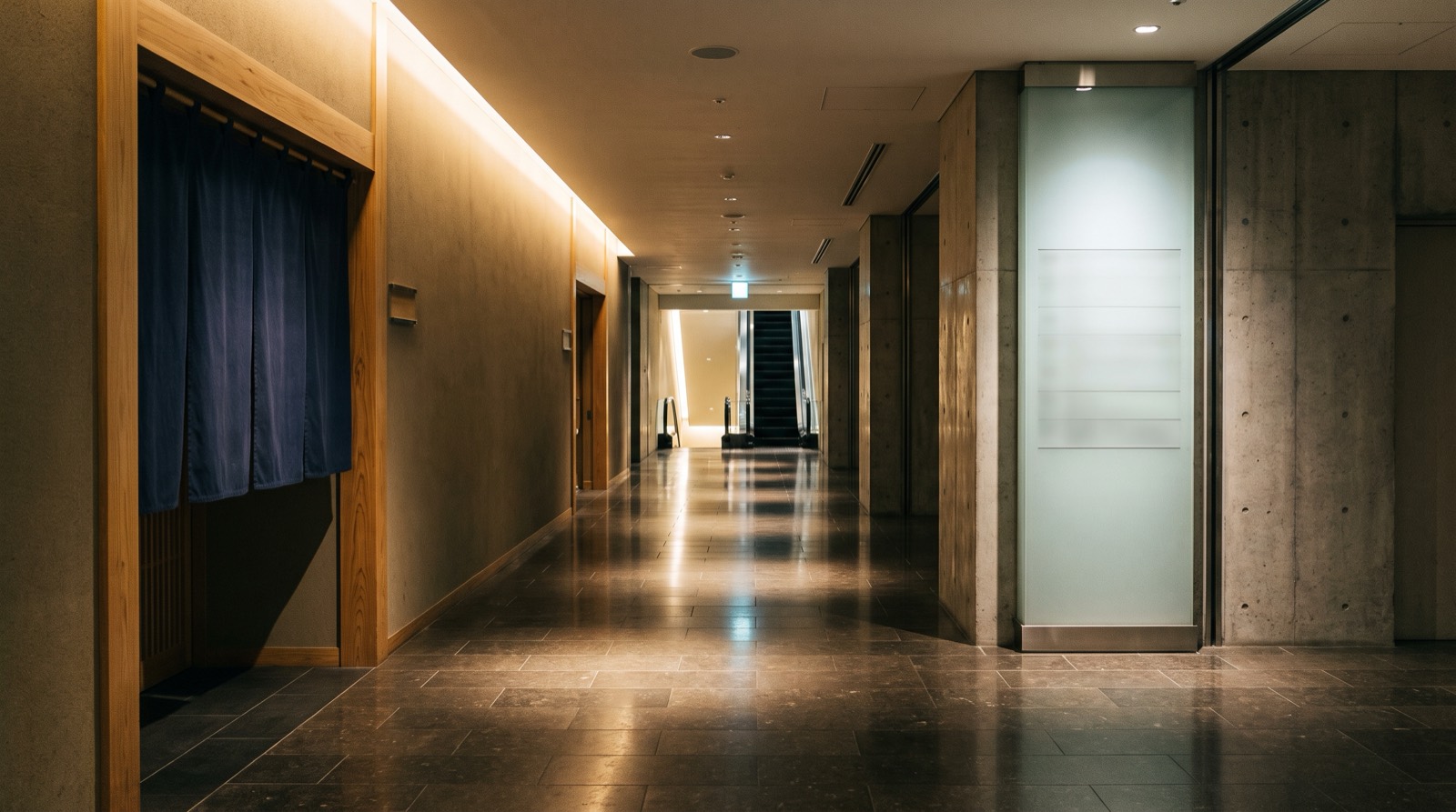 A basement arcade corridor, a shop curtain on the left and a tall directory panel on the right.