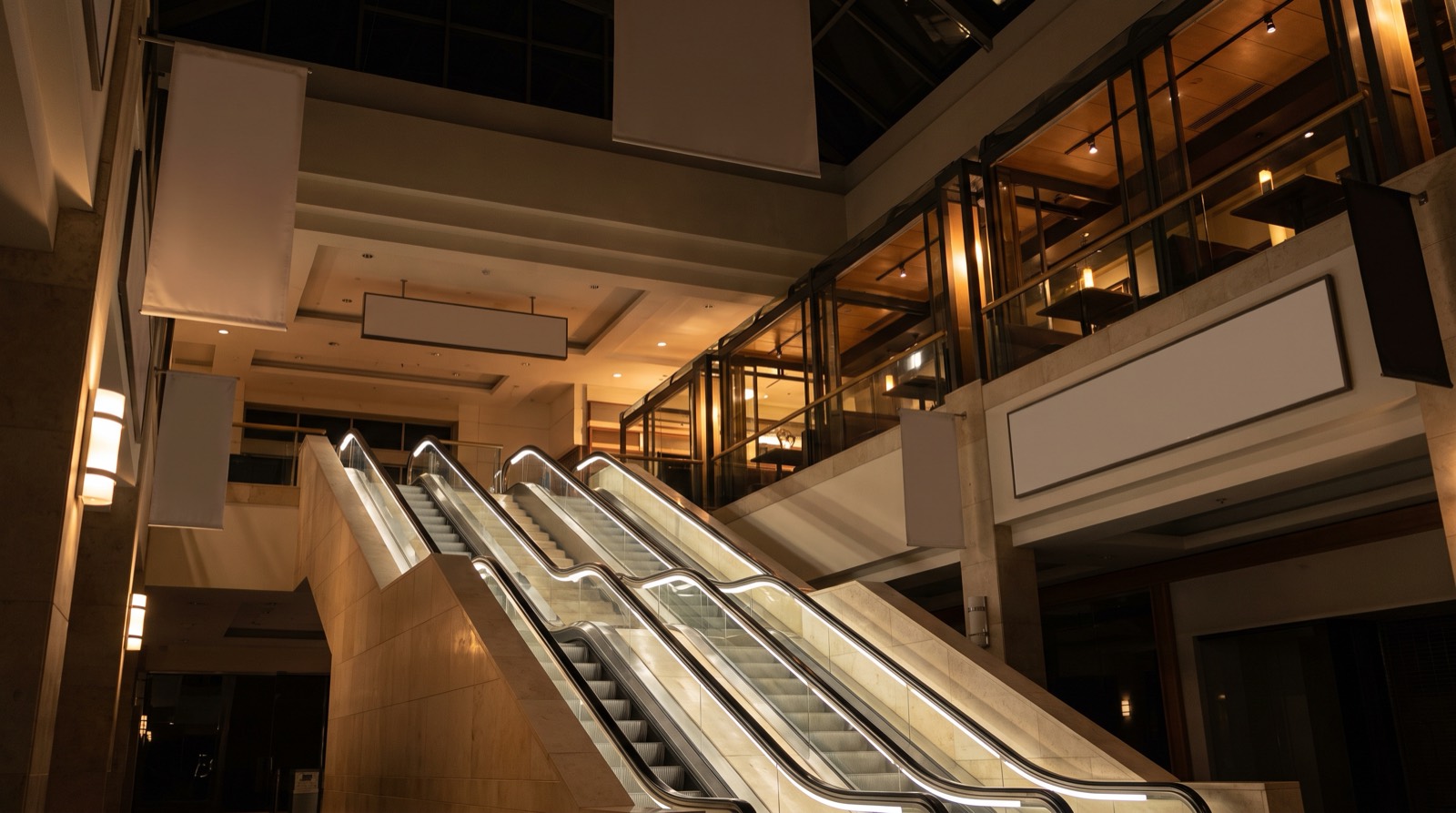 An escalator rising through the atrium of a station-side building, restaurant floors lit above.