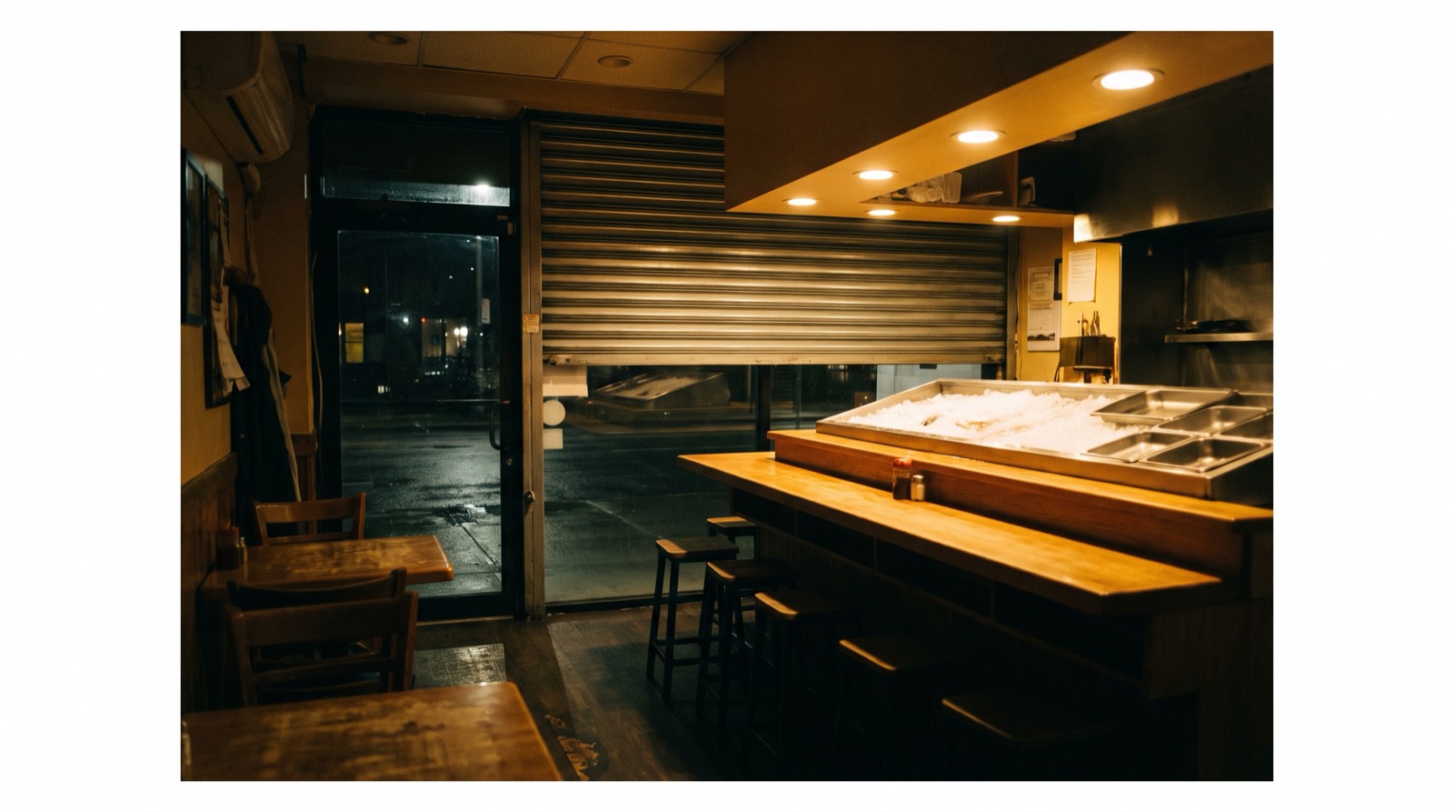 A counter lit late, the shutter half drawn behind it.