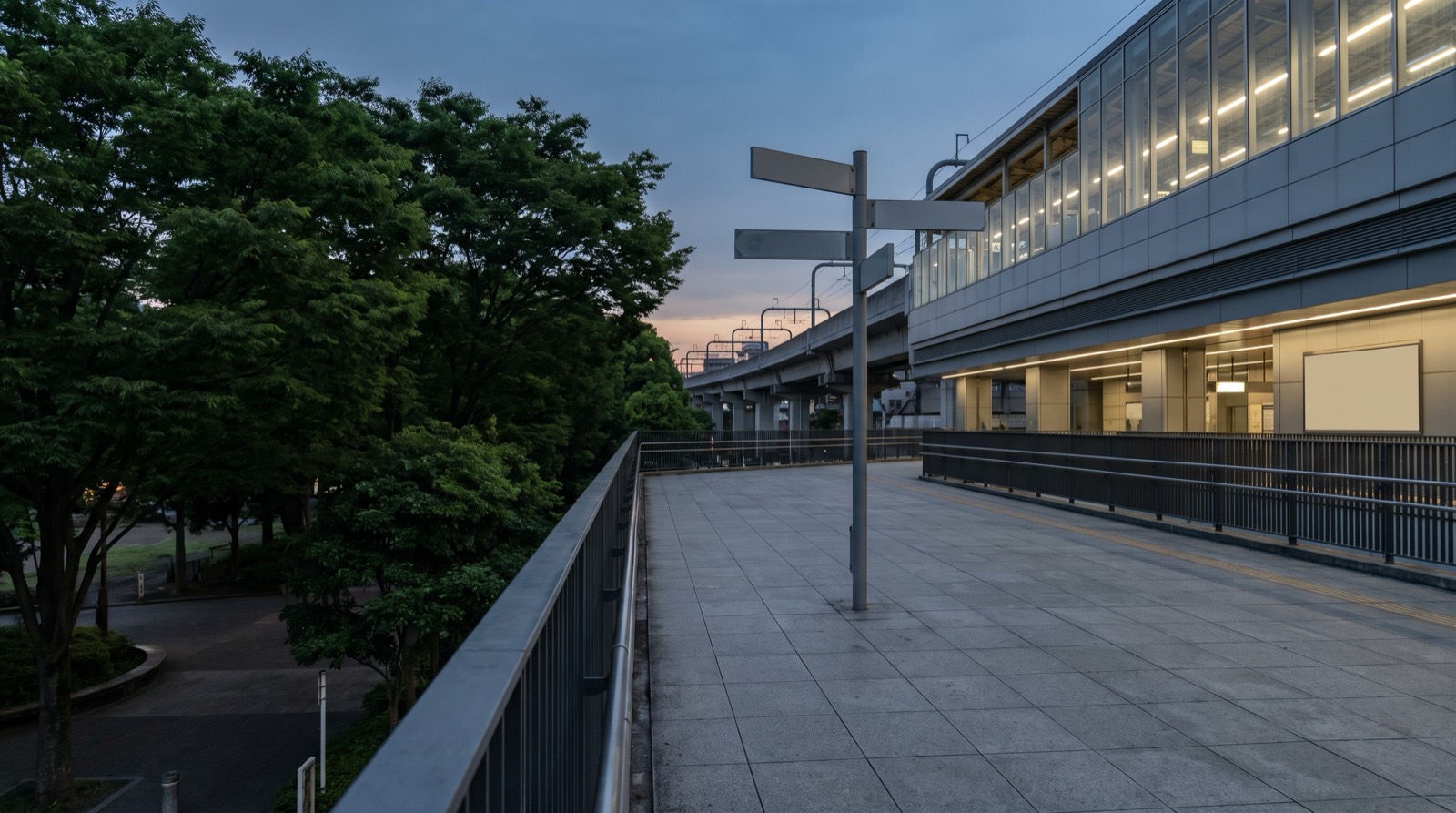 A station-side pedestrian deck at dusk, a multi-armed direction post standing on it.